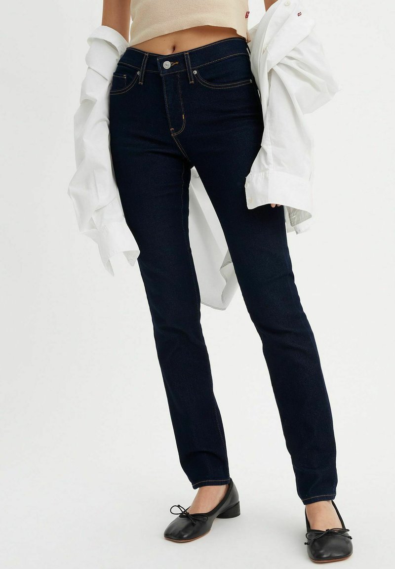 Mörkblå skinny jeans med hög midja, kontrasterande sömmar och femficksdesign. Bärs med en lös, vit skjorta och svarta lägenheter.