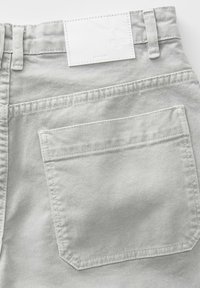 Jeans in denim grigio chiaro con tasca posteriore a toppa e etichetta bianca semplice in vita, con dettagli di cucitura visibili.