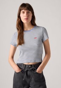 Svītraina T-krekls zilā un baltā krāsā ar rievotu tekstūru un apaļu kakla izgriezumu. Uz krūtīm maza sarkana logo. Kombinēts ar augsta jostas melnām džinsu biksēm.