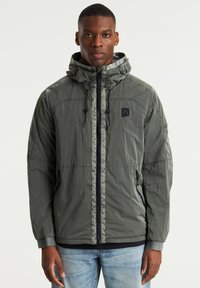 Chaqueta con capucha gris hecha de material ligero, con cremallera completa, capucha ajustable y bolsillos laterales. Acabado texturizado con parche de logo.