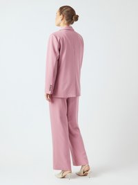 Vaaleanpunainen puku, jossa on räätälöity takki ja leveälahkeiset housut. Silkkinen kangas, jossa on hienovarainen pinta, yhdistettynä teräväkärkisiin valkoisiin korkokenkiin.