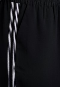 Čierna látka s elastickým pásom a tromi zvislými bielymi pruhmi vedúcimi po boku.