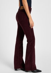 Burgundy flared corduroy jeans with a smooth texture, five-pocket design, and branded brown leather patch at the waist. Points for subtle stitching.