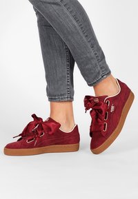 Baskets en daim rouge avec de larges lacets en satin, semelles en caoutchouc et œillets métalliques. Accentuées de finitions blanches et d'un logo sur le côté.