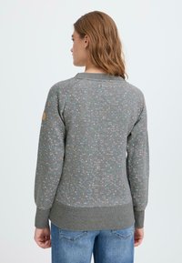 Sudadera gris con lunares en tonos pastel, puños y dobladillo acanalados, y un cuello redondo. La tela parece suave y tiene un ajuste relajado.