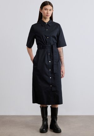 Marineblaue Hemdblusenkleid mit kurzen Ärmeln, tailliertem Bindegürtel, Seitentaschen und glattem Stoff, kombiniert mit kniehohen schwarzen Stiefeln.