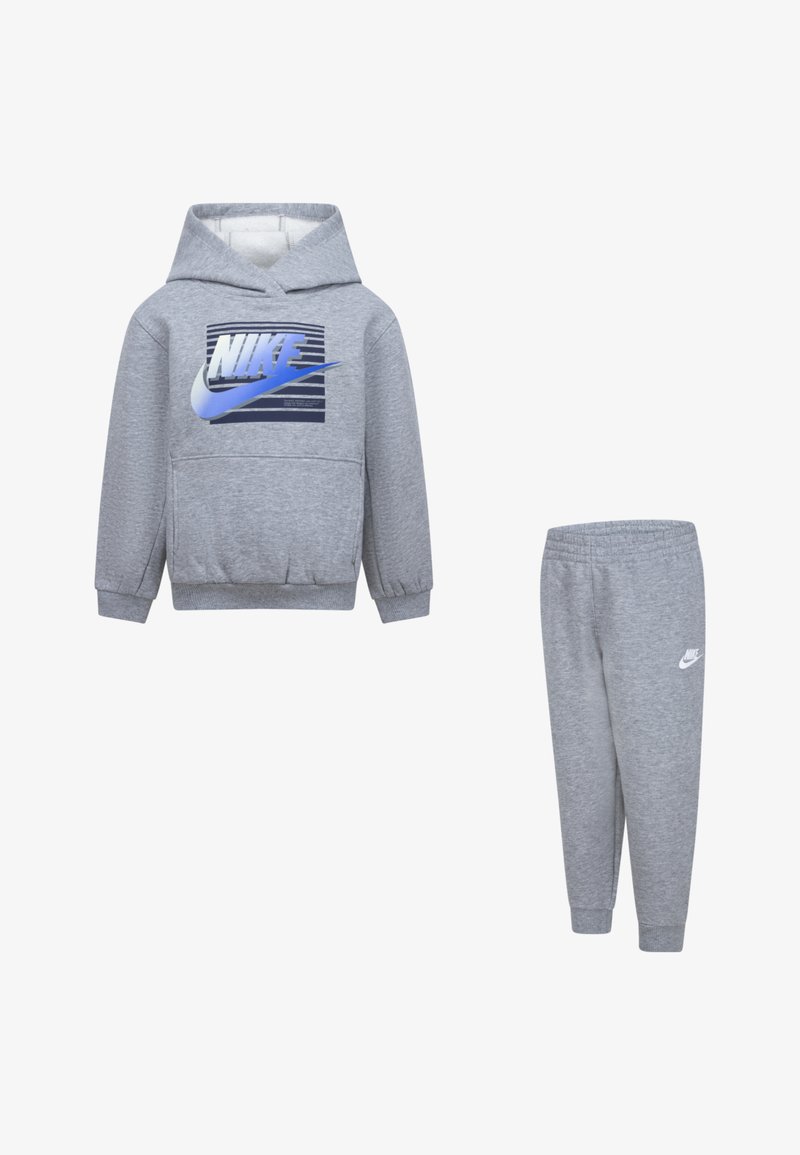 Moleton cinzento com bolso frontal e logotipo azul da Nike, combinado com calças de fato cinzentas com um pequeno logotipo branco da Nike. Textura macia.