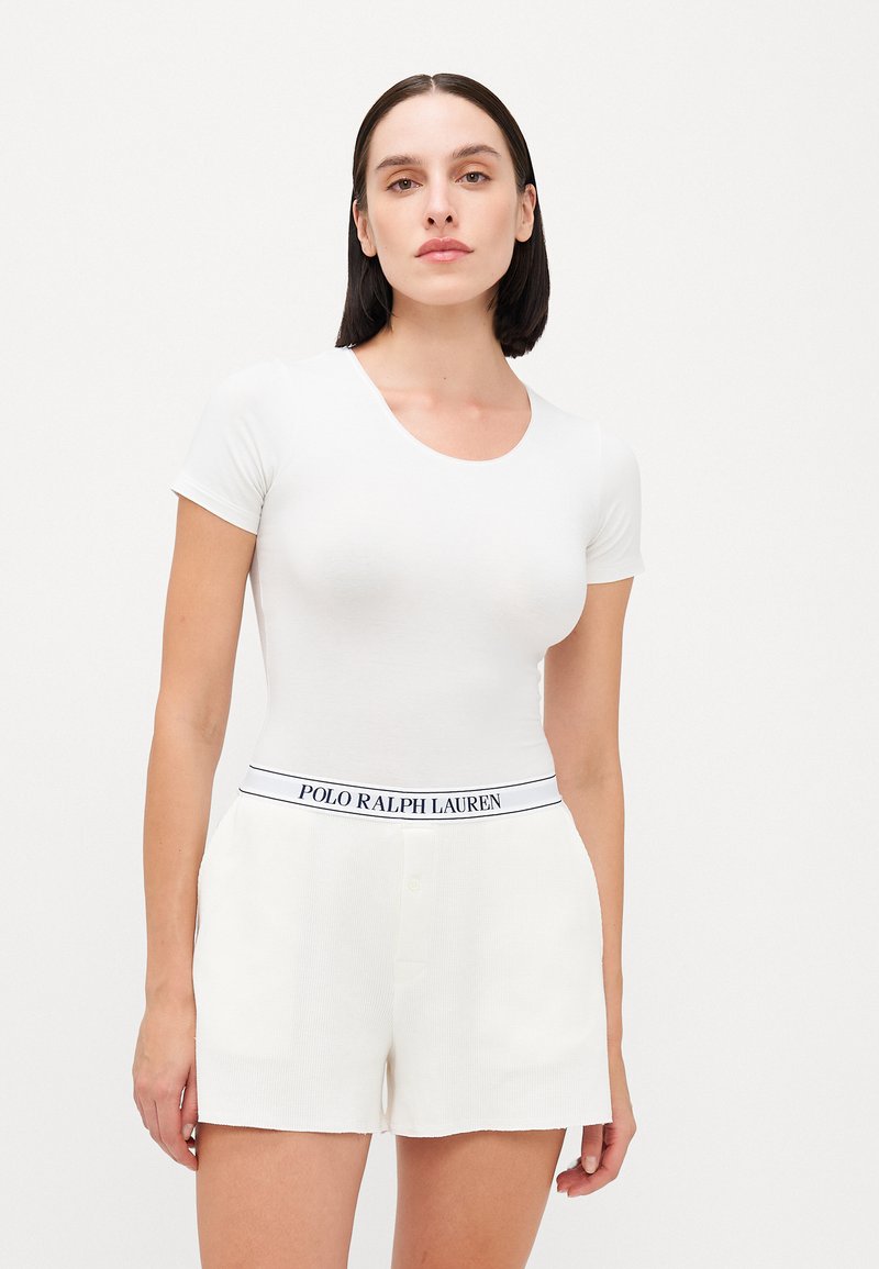 White short-sleeve fitted top paired with cream shorts featuring a blue "POLO RALPH LAUREN" waistband and button detail. Smooth fabric texture.