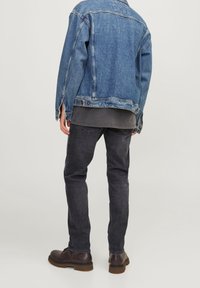 Denim jack, vervaagd blauw, losse pasvorm met zijsplitten; grijs shirt eronder, zwarte spijkerbroek en bruine veterschoenen met een rubberen zool.