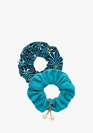 Kobieta w turkusowym bikini z góry wiązanym na szyi i dopasowaną gumką do włosów, pozująca z ręką dotykającą szyi, patrząca w bok na tle jednolitym.