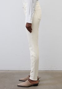 Jeans blancos ajustados con una textura suave, que cuentan con bolsillos laterales y una cinturilla estándar, combinados con zapatos de tacón bajo grises.