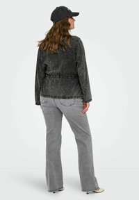 Temno siva jeans jakna z dolgimi rokavi in raztrganim robom. Ujemajoče svetlo sivo široko krojene kavbojke. Model nosi črno kapo. Vidne so gladke teksture.