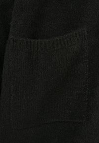 Tuvplāns melnai adītai kabatai ar ribotu apmalējumu uz mīksta, teksturēta apģērba.