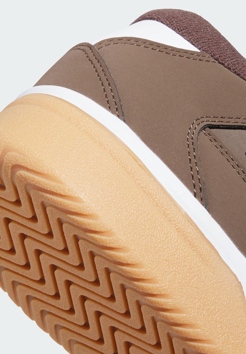 Brown athletic sneaker featuring a textured rubber sole with a zigzag pattern, smooth synthetic upper, and white accents.