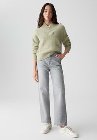 Hellgrüner, strukturierter Strickpullover mit weitem Ausschnitt, kombiniert mit grauen, hochgeschnittenen, geraden Jeans. Schuhwerk: weiße Sneaker.