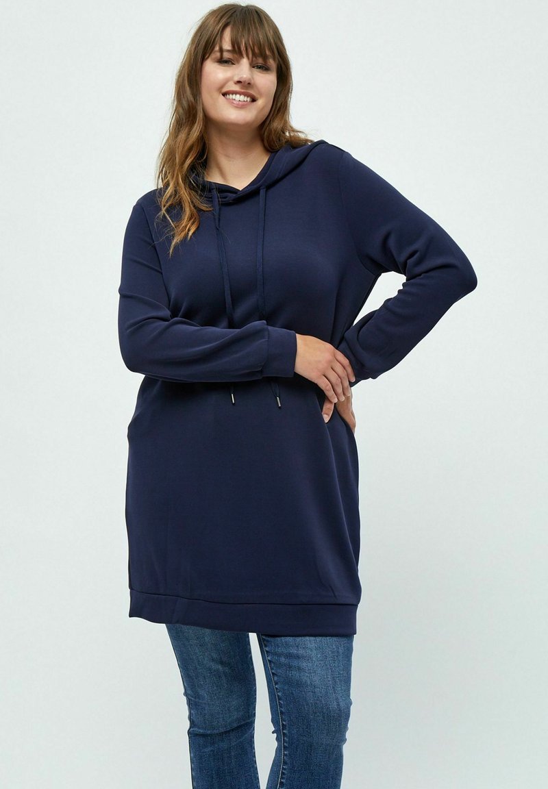 Dunkelblaues Kapuzensweatshirt aus weichem Material, mit langen Ärmeln, einer Fronttasche und einem rund ausgeformten Saum, kombiniert mit blauen Jeans.