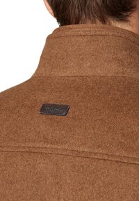 Brązowa kurtka z wełnianego materiału z podniesionym kołnierzem, z skórzaną metką na plecach oznaczoną "LANCERTO". Teksturowana tkanina z widocznym szwem.