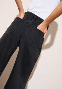 Fekete, bő szárú farmernadrág, klasszikus hátulsó zsebekkel. Az anyag enyhén textúrált, matt felületű.