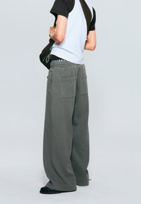 Pantaloni de trening gri largi, cu un șnur la talie și două buzunare mari la spate, asortați cu un tricou scurt cu mânecă alb-negru și pantofi negri.