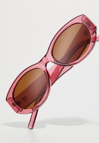 Rosa acetat solbriller med store runde linser, brun tone og en noe transparent ramme. Distinkt geometrisk form og solide armer.