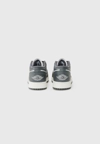 Baskets en cuir gris avec des semelles blanches, dotées d'un col rembourré, de coutures décoratives et d'un logo bien visible au niveau du talon.