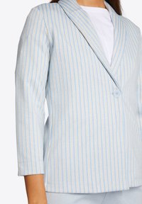 Lichtblauwe blazer met verticale witte en gouden strepen, met enkele knoopsluiting, met gesneden revers en driekwartmouwen. Hondenstof.