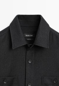 Schwarzes Wollhemd mit spitzem Kragen, zwei Brusttaschen und Knopfleiste, ausgestattet mit vier schwarzen Knöpfen und einer weichen, strukturierten Oberfläche.