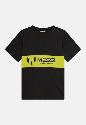 Melna kokvilnas T-krekls ar platām dzeltenām svītrām pāri krūtīm, kurā ir teksts "MESSi" un "TRAINING SYSTEM" treknās melnās burtos.