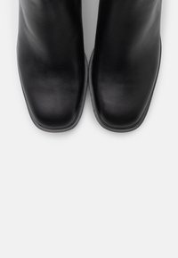 Bottines en cuir noir avec un bout carré, une texture lisse et un design minimaliste, dotées d'une semelle discrète et sans éléments métalliques apparents.