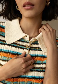 Pletený svetřík s límečkem s vodorovnými pruhy v oranžové, modré a hnědé barvě; má dva knoflíky, strukturovanou látku a světle krémový límec.