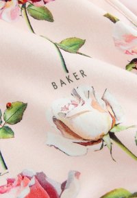 Tessuto rosa tenue con rose bianche e rosa stampate, foglie verdi e la parola "BAKER" visibile vicino a una rosa bianca.