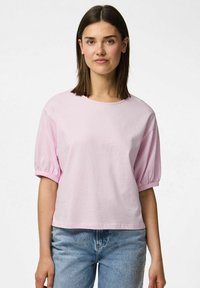 Vaaleanpunainen lyhythihainen croppit-paita, jossa on puffy hihat ja pyöreä kaula-aukko. Valmistettu pehmeästä puuvillakankaasta. Rennon mallinen. Vaaleansiniset farkut.