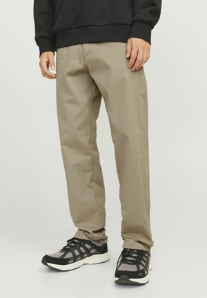 Beige katoenen broek met een rechte pijp, gecombineerd met zwart en grijs sport schoenen met gaasdetails en reflecterende accenten.