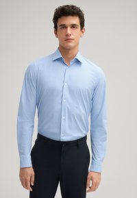 Lichtblauw overhemd met lange mouwen en een subtiel patroon. Kenmerken zijn een klassieke kraag en een getailleerde pasvorm. Gepaard met donkere broek.