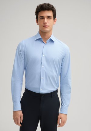 Chemise boutonnée à manches longues bleu clair avec un motif subtil. Dotée d'un col classique et d'une coupe ajustée. Associée à un pantalon sombre.