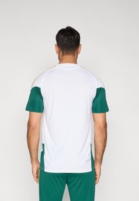 Biely športový dres so zelenými rukávmi a detailmi. Má okrúhly výstrih a jemné zlaté prvky pozdĺž ramenných švov.