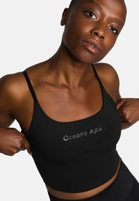 Zwarte crop top met spaghettibandjes, gemaakt van een zachte stof en voorzien van geborduurde tekst "Oceans Apart" in zilver. Eenvoudig, aansluitend ontwerp.