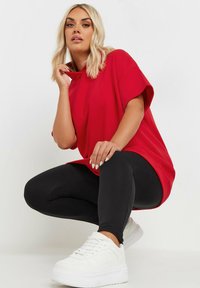 Röd oversize T-shirt med hög halsringning, tillsammans med svarta leggings och vita plattformssneakers. Slätt tyg, avslappnad passform, korta ärmar.