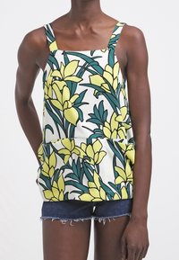 Ärmelloses Top mit Blumenmuster in Gelb und grünen Blättern auf weißem Hintergrund, kombiniert mit Jeansshorts. Strukturierter Stoff.