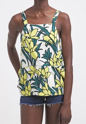 Haut sans manches à motifs floraux avec des fleurs jaunes et des feuilles vertes sur un fond blanc, associé à un short en denim. Tissu texturé.