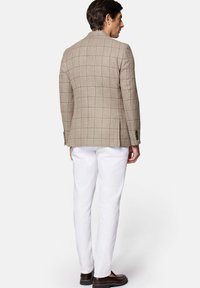 Beżowa marynarka w kratę o dopasowanym kroju, zestawiona z białymi spodniami. Wyraziste detale to zapinane mankiety i fakturowany materiał.