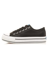 Zapatilla de lona negra con puntera y suela de goma blanca, que presenta rayas negras, ojales de metal y un acento de logo azul en el talón.