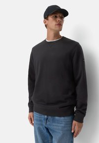 Zwarte katoenen sweatshirt met een ronde halslijn, ribbelmanchetten en -zoom. Gecombineerd met lichtblauwe denim jeans en een bijpassende zwarte baseballcap.