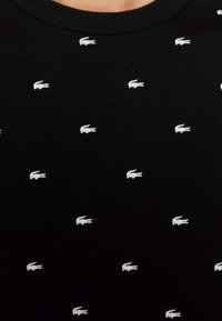 Sort bomulds T-shirt med et gentaget mønster af en hvid krokodille-logo. Rund hals, blød tekstur og korte ærmer.