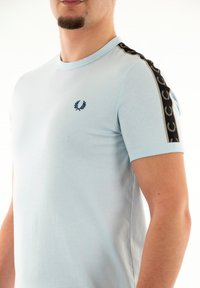 Camiseta de manga corta azul claro de algodón suave, con paneles laterales negros con acentos estampados y un logo azul marino en el pecho.