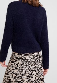 Dark navy fuzzy sweater with a relaxed fit, paired with a beige skirt featuring a black animal print pattern. Textured fabric visible.