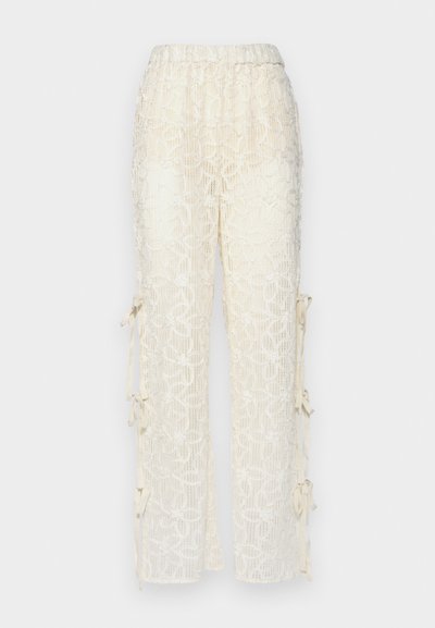 Pantalons en dentelle couleur crème avec une taille élastique, ornés de motifs floraux et de liens sur les côtés pour un ajustement réglable.