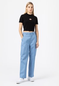 Black cropped t-shirt with logo, paired with high-waisted light blue trousers. Model wears white sneakers. Simple, minimalistic design.