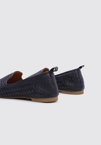 Zapatos planos de color azul marino con un patrón texturizado, laterales abiertos y una suela de goma beige. Incluyen un pequeño bucle en el talón para facilitar su uso.