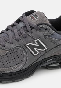 Gros plan d'une basket New Balance grise avec des panneaux en daim et en mesh, une semelle noire, des lacets gris, et le logo "N" de la marque sur le côté.